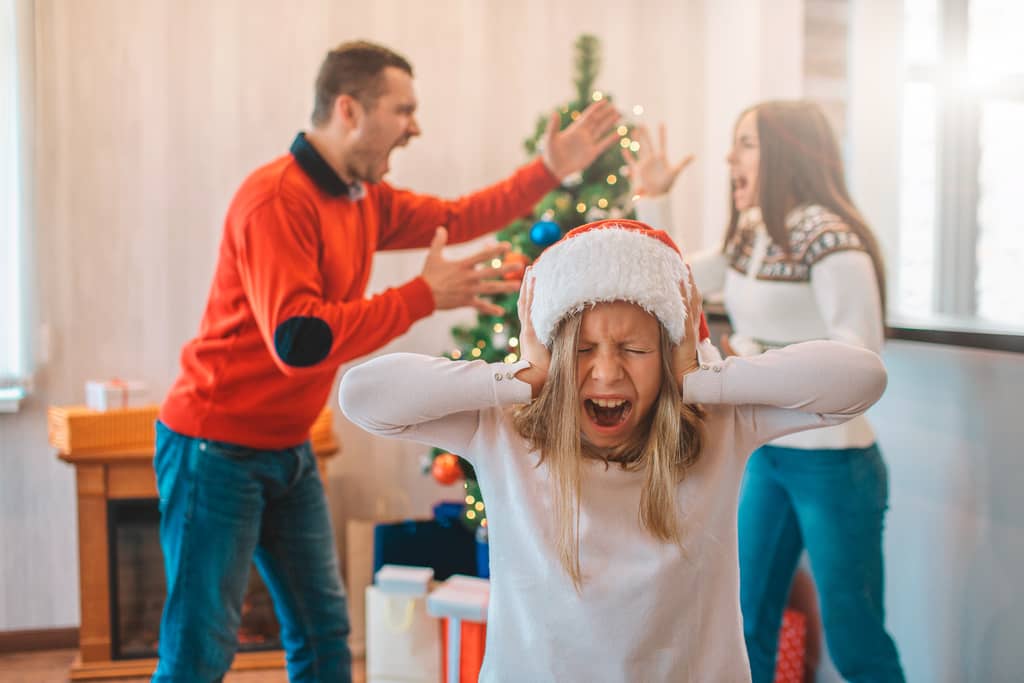 Mann und Frau streiten sich zu Weihnachten und die Tochter hält sich die Ohren zu.